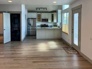 Kitchen with glass insert cabinets, a peninsula, stacked washer / drying machine, baseboards, and appliances with stainless steel finishes