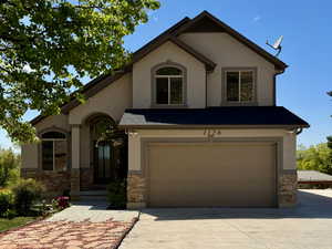 View of front of home featuring an attached garage, stone siding, concrete driveway, and stucco siding
