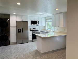 Kitchen with stainless steel appliances, a peninsula, a sink, a textured ceiling, and stacked washing maching and dryer
