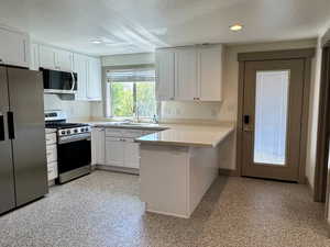Kitchen featuring recessed lighting, stainless steel appliances, a peninsula, a textured ceiling, and white cabinetry