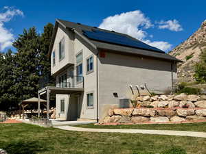View of home's exterior featuring stucco siding, solar panels, a yard, and a balcony