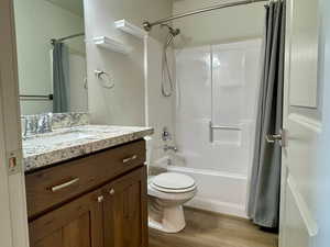 Full bath with shower / bath combo, a textured ceiling, toilet, wood finished floors, and vanity