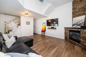 Living area featuring a stone fireplace, stairs, wood finished floors, and baseboards