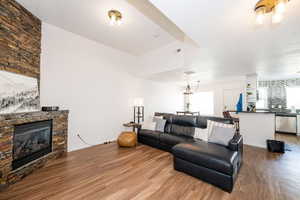 Living room with a stone fireplace, wood finished floors, visible vents, and baseboards