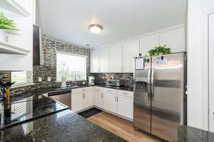 Kitchen featuring white cabinets, a sink, dark stone counters, decorative backsplash, and appliances with stainless steel finishes