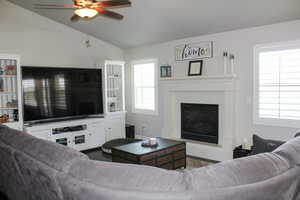 Living area featuring ceiling fan, vaulted ceiling, a wealth of natural light, and a glass covered fireplace