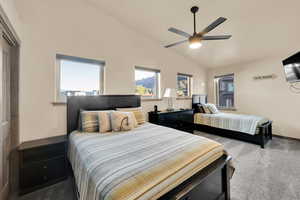 Carpeted bedroom featuring ceiling fan, vaulted ceiling, and multiple windows