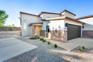 Contemporary house featuring stucco, stone siding, a garage, and fence