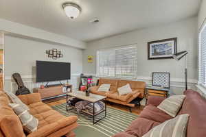 Living area with a wainscoted wall, wood finished floors, and visible vents