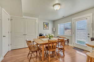 Dining room with baseboards, a textured ceiling, visible vents, and light wood-style flooring