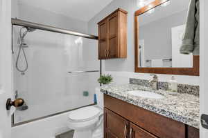 Bathroom with toilet, vanity, and combined bath / shower with glass door