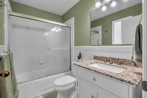 Bathroom with wainscoting, vanity, enclosed tub / shower combo, toilet, and tile patterned flooring