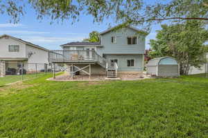 Back of house featuring stairway, a lawn, fence, a wooden deck, and a storage unit