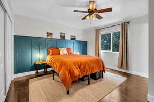 Bedroom featuring wainscoting, dark wood finished floors, and ceiling fan