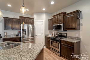 Kitchen featuring dark brown cabinetry, appliances with stainless steel finishes, a sink, and light wood-type flooring