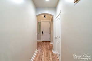 Hallway with light wood-style flooring, baseboards, and arched walkways