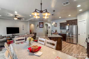 Dining space with arched walkways, light wood-style floors, visible vents, and ceiling fan with notable chandelier