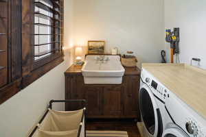 Laundry area featuring washing machine and clothes dryer, dark wood-style flooring, a sink, and cabinet space