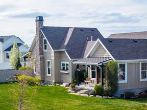 Back of house featuring a patio area, a lawn, a chimney, a shingled roof, and fence