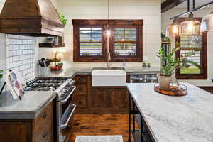 Kitchen featuring a sink, dark wood-style flooring, custom range hood, light stone countertops, and appliances with stainless steel finishes