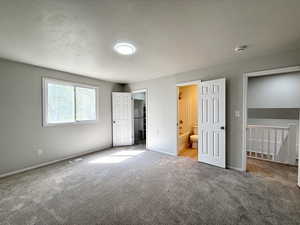 Unfurnished bedroom with a spacious closet, visible vents, carpet floors, ensuite bath, and baseboards
