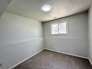 Spare room featuring baseboards, dark colored carpet, a textured ceiling, and visible vents