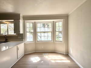 Unfurnished dining area with crown molding, a sink, visible vents, and light wood-type flooring
