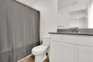 Full bathroom with wood finished floors, vanity, shower / tub combo with curtain, toilet, and visible vents
