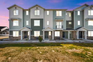 Townhome / multi-family property featuring board and batten siding, a lawn, stone siding, and a balcony