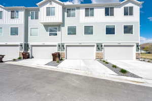 Townhome / multi-family property featuring board and batten siding, driveway, stone siding, and a garage