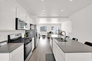 Kitchen with dark countertops, a sink, a kitchen island with sink, light wood-style flooring, and appliances with stainless steel finishes