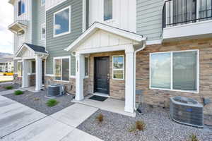 Doorway to property with board and batten siding, cooling unit, and stone siding
