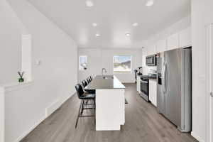 Kitchen with white cabinets, a kitchen breakfast bar, a sink, a center island with sink, and appliances with stainless steel finishes