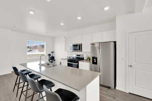 Kitchen with a sink, light wood-style floors, a breakfast bar, stainless steel appliances, and a center island with sink