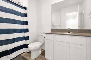 Full bath with a shower with shower curtain, wood finished floors, toilet, and vanity