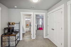 Hallway featuring carpet floors, a textured ceiling, visible vents, and baseboards