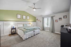 Carpeted bedroom with vaulted ceiling, visible vents, baseboards, and ceiling fan