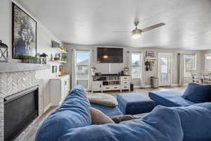 Living room featuring baseboards, a fireplace, light wood-style flooring, a textured ceiling, and ceiling fan