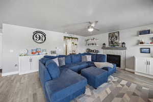 Living room with light wood finished floors, a textured ceiling, baseboards, a ceiling fan, and a tile fireplace