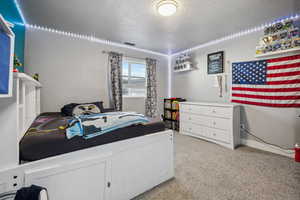 Bedroom with a textured ceiling, light colored carpet, and visible vents