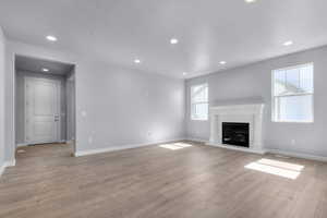 Unfurnished living room featuring baseboards, a glass covered fireplace, light wood finished floors, and recessed lighting
