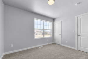 Unfurnished bedroom featuring carpet floors, a textured ceiling, visible vents, and baseboards