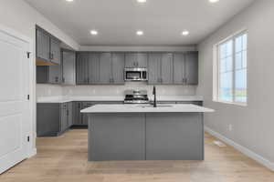 Kitchen featuring a sink, light wood-style floors, a kitchen island with sink, light countertops, and appliances with stainless steel finishes