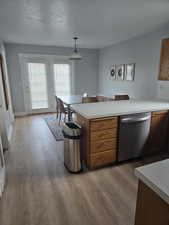 Kitchen featuring dishwasher, light countertops, a peninsula, brown cabinetry, and light wood finished floors