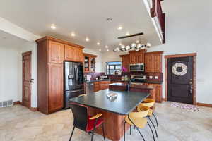 Kitchen with dark countertops, tasteful backsplash, an island with sink, appliances with stainless steel finishes, and visible vents