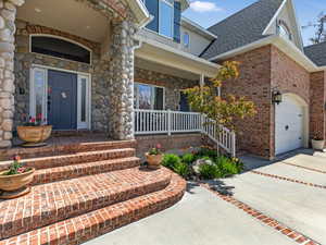 Entrance to property with covered porch, a garage, driveway, and roof with shingles