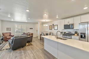 Kitchen with a sink, open floor plan, stainless steel appliances, light wood-style flooring, and a notable chandelier