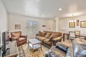 Living area featuring baseboards, a chandelier, light wood finished floors, and a textured ceiling