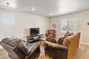 Living area with light wood-style flooring, baseboards, a textured ceiling, and recessed lighting