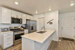 Kitchen with white cabinets, light wood-type flooring, stainless steel appliances, and a sink